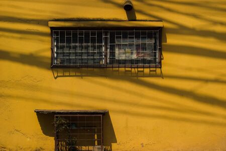 Yellow wall with a steel cage window and a wooden plate under it