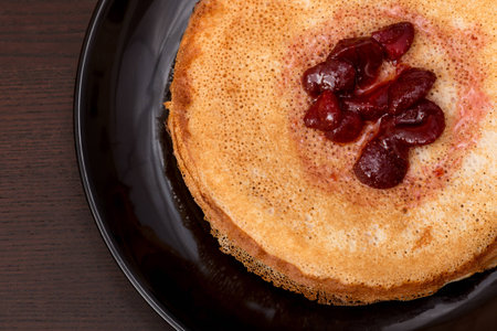 Pancakes with strawberry jam on a black plateの写真素材