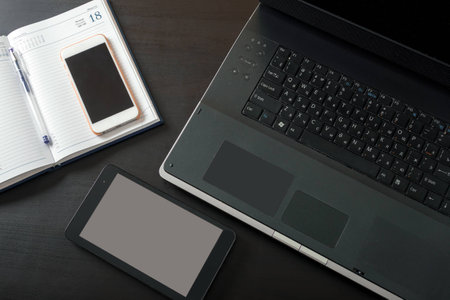 Laptop, tablet, mobile phone, notebook, lying on a black tableの写真素材