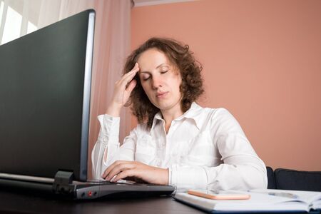 tired woman with a headache using a laptopの写真素材