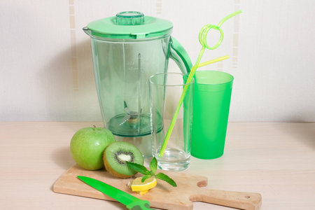 Cooking smoothie of kiwi, apple, lemon and mint. Blender, knife, glasses, straw and wooden boardの写真素材