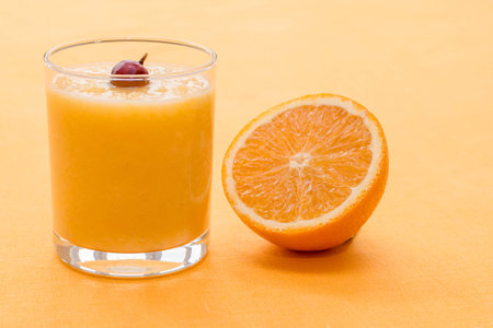 Orange smoothie with a gooseberry  in a glass on orange backgroundの写真素材