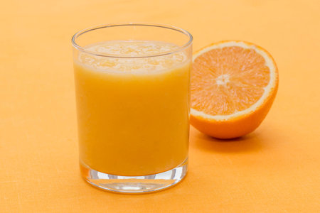 Orange smoothie in a glass on an orange backgroundの写真素材