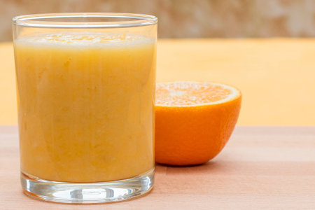 Orange smoothie in a glass on an orange backgroundの写真素材