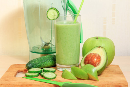 Green smoothie with apple, avocado and cucumber in a glass, blener and knifeの写真素材