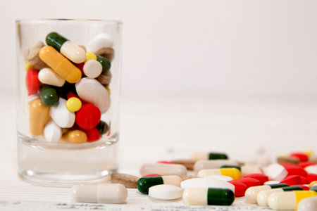 Bunch of various color pills in glass in on white table 