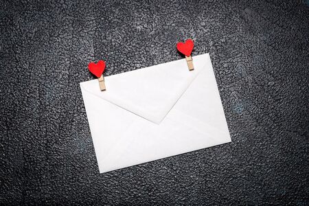 White envelope with clothes pegs with hearts on a dark backgroundの写真素材