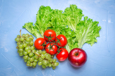 Top view of health food: tomato, apple, grape, salad on blue background. Healthy eating conceptの写真素材