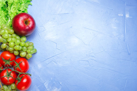 Top view of health food: tomato, apple, grape, salad on blue background with space for text. Healthy eating conceptの写真素材