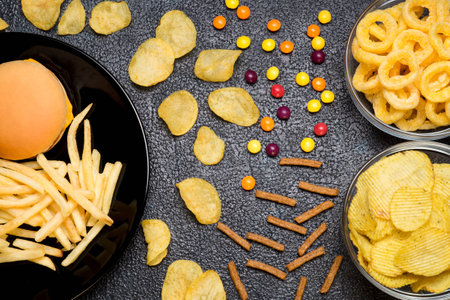 Fast food: top view of burger, french fries, chips, rings and candies on dark background. Unhealthy eating concept の写真素材