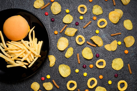 Fast food: top view of burger, french fries, chips, rings and candies on dark background. Unhealthy eating concept の写真素材