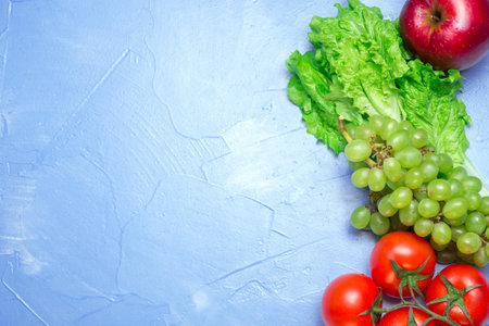 Top view of health food: tomato, apple, grape, salad on blue background with space for text. Healthy eating conceptの写真素材