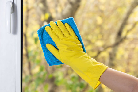 Hand in yellow glove cleaning window with blue ragの写真素材