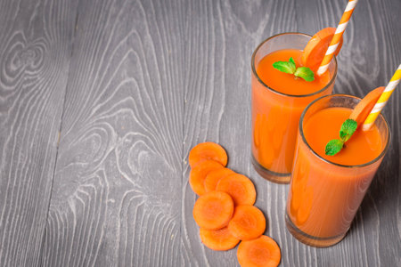 Carrot smoothie with ingredients on gray wooden background with copyspaceの写真素材