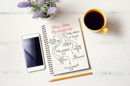 New year resolution in notebook with flower, pen, coffee and phone on white wooden deskの写真素材