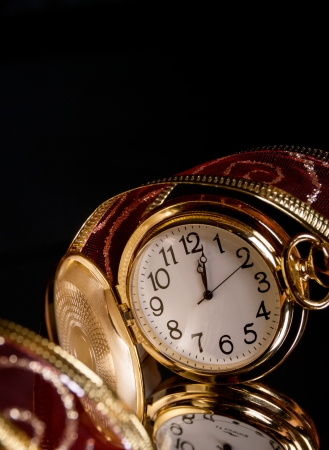 round gold watch with a tracery a red ribbon on a black background with reflectionの写真素材