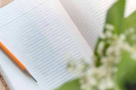 pencil on the open notebook with lilies of the valleyの写真素材