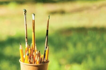 Paper cup with paint brushes and pencils on a green backgroundの写真素材