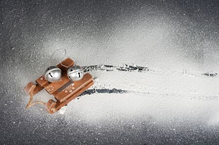 wooden sled toy in the snow, track in the snow from the sled, silver bells on the sled, top view, white snow on a black backgroundの写真素材