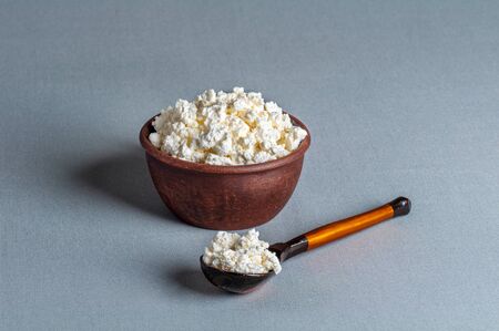 cottage cheese in a clay plate and wooden spoon, on a gray backgroundの写真素材