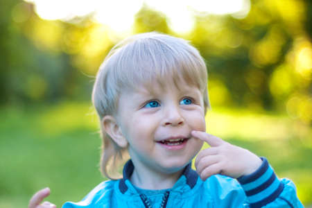 blonde and white-skinned toddler laughs at the camera in the spring on the street