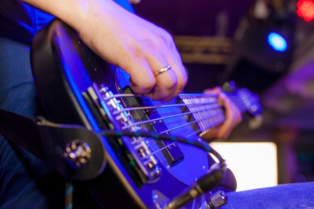 Musician plays bass guitar on stage in neon light close upの写真素材