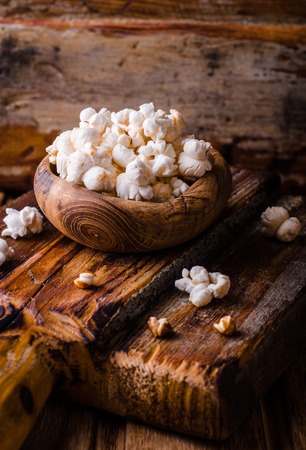 Wooden bowl full of sweet caramel popcorn with icing sugar and corncobs over rustic table. Vintage style. Selective focusの写真素材