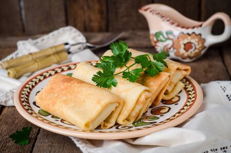 Stuffed russian pancakes rolls with meat in traditional clay bowl on wooden background.