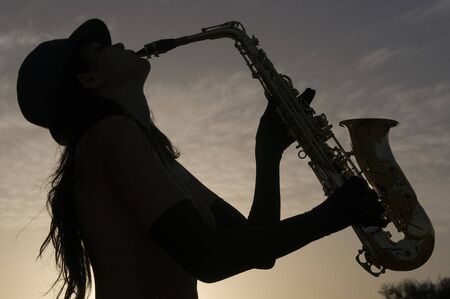 silhouette of a woman playing saxofon under the skyの写真素材