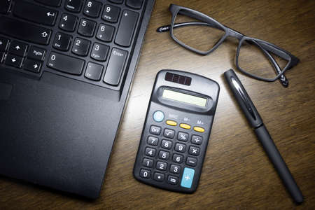 The glasses with the laptop , the calculator and the pen on the brown wooden working table.の写真素材