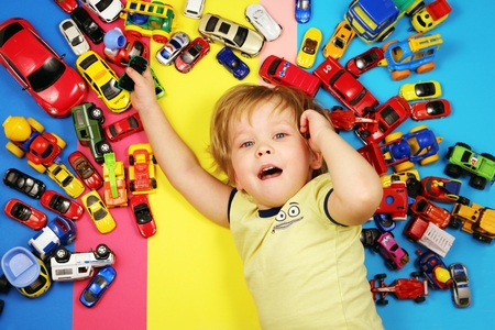 Baby boy on multicolored background surrounded by toy carsの写真素材