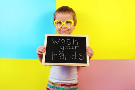 Wash your hands. Health care concept. Happy boy holding a blackboard with text messageの写真素材