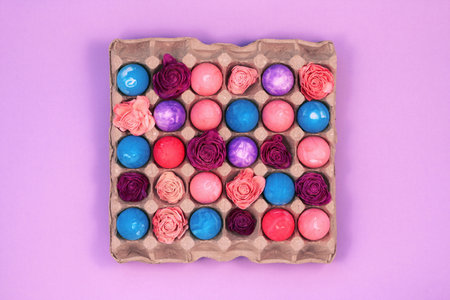 Easter eggs painted with gouache and flowers in egg box on violet pink background, top viewの写真素材