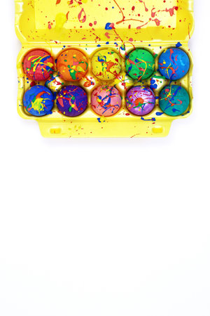 Bright Easter eggs painted with gouache in yellow egg box isolated on white background, top view copy space, vertical imageの写真素材