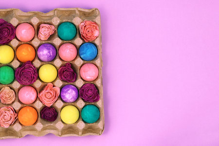 Multicolored Easter eggs painted with gouache and flowers in egg box on violet pink background, top view copy spaceの写真素材