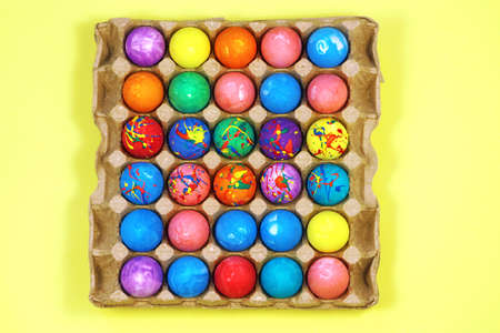 Many multicolored easter eggs in egg carton box on yellow background top viewの写真素材