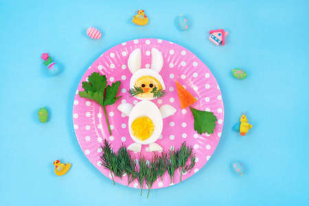 Breakfast idea for kids. Bunny rabbit made of boiled eggs on pink plate, blue background, top viewの写真素材