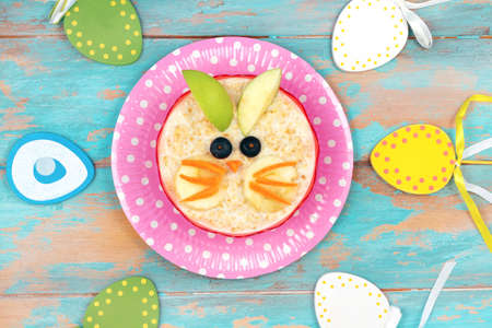 Funny breakfast for kids. oatmeal with fruits. blue wooden background, top view. Easter breakfast idea for childrenの写真素材