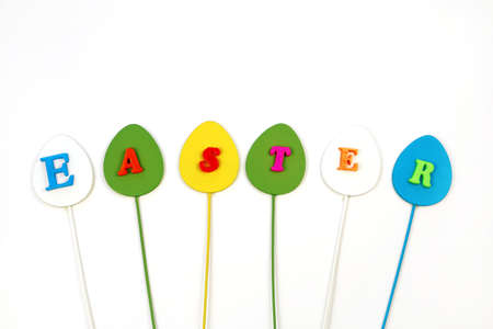 Word Easter isolated on white background, copy space, minimalism. Inscription Easter on multicolored egg sticks.の写真素材