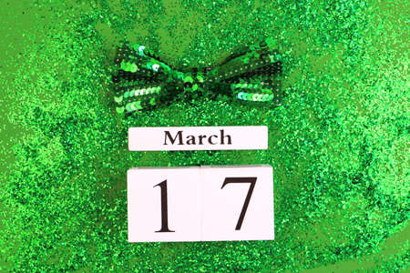 Saint Patricks Day greeting card. Block calendar and bow tie on green glitter sequins background.の写真素材