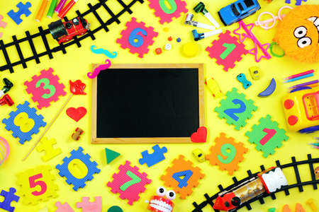 Blackboard surrounded by many different childrens toys and numbers on yellow background. Early childhood education concept, preschool.の写真素材