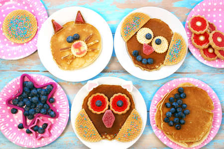 Funny pancakes for children. Cat, dog and owl shaped pancakes on white plates, blue wooden background, top view. Creative idea for kids breakfast.の写真素材