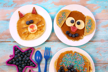 Fun food for children. Cat and dog shaped pancakes on white plates, blue wooden background, top view. Creative idea for kids breakfast.の写真素材