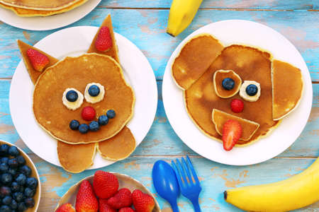 Fun food for kids. Cat and dog shaped pancakes with berries on blue wooden table, top view. Healthy vegetarian food for children.の写真素材