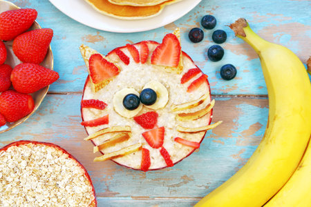 Fun food for kids - cute oatmeal cat tiger on blue wooden table, top view. Healthy vegetarian eating for childrenの写真素材