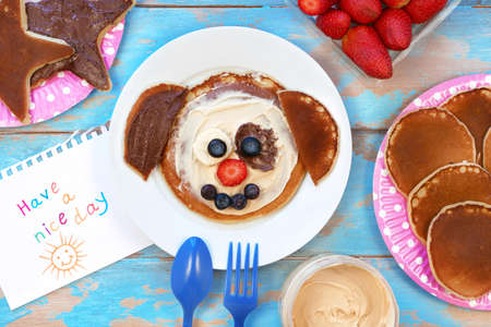 Fun food for kids. Dog shaped pancakes with berries and peanut paste on blue wooden table, top view. Healthy vegetarian food for children.の写真素材