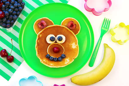 Fun idea for kids breakfast. Bear shaped pancakes with berries on green plate, top view. Healthy food for children. Funny food for kids.の写真素材