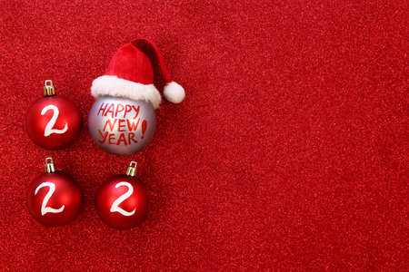 New year 2022 celebration concept. Christmas ball in santa hat on red glitter background copy space....