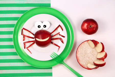 Fun food for kids. Cute smiling spider or crab made from red apple. Oatmeal porridge with apple slices. Healthy breakfast for childrenの写真素材