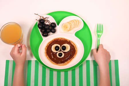 Fun food for kids. pancakes with grapes and banana in a rabbit-shaped plateの写真素材